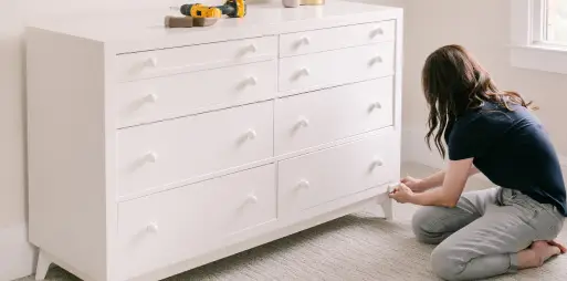 Baby proofer installing corner cushions on a dresser