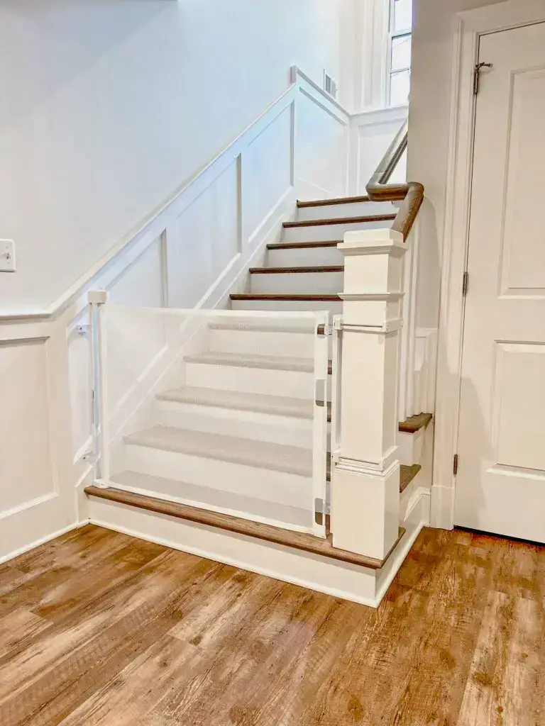White retractable gate installed on basement stairs going up with oversized post clamps, locked and engaged.