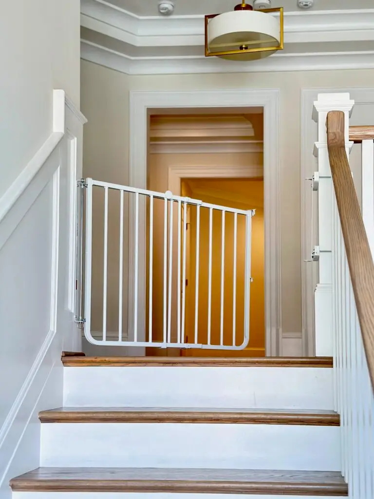 White stairway gate installed in second floor hallway, slightly ajar.