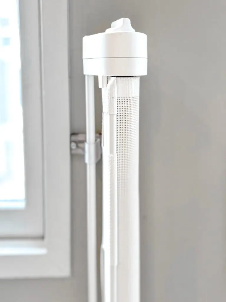 Close-up of a white retractable mesh gate housing mounted beside a window frame