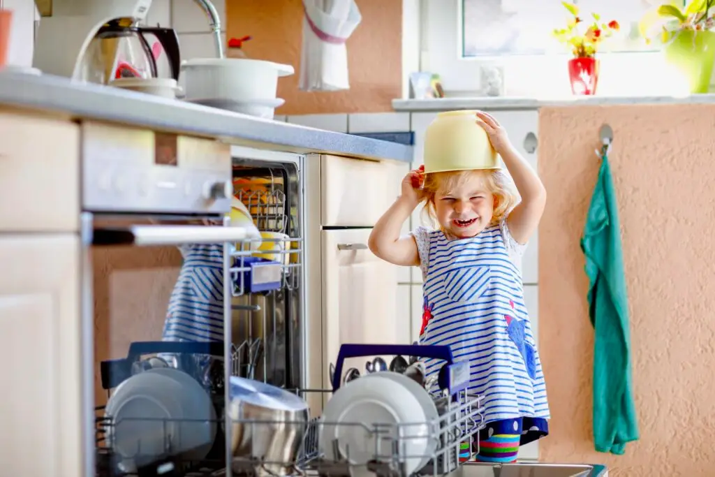 Toddler in kitchen playing with bowl on her head.
