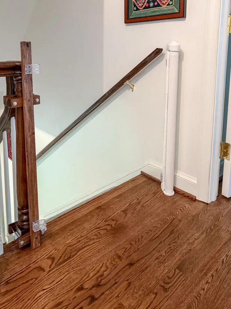 Retractable gate retracted open at the top of the stairs beside a dark-stained newel post