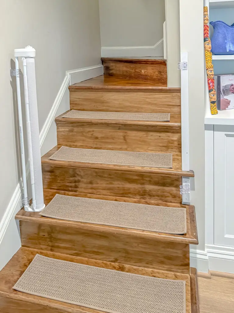 Retractable gate retracted open at the top of wood stairs with carpet treads
