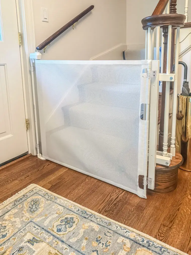 White retractable gate closed at the bottom of a staircase with turned balusters and a blue-bordered runner in a bethesda, md home