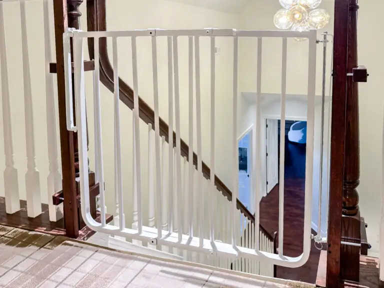 White stairway gate installed across the top of a staircase with dark newel posts