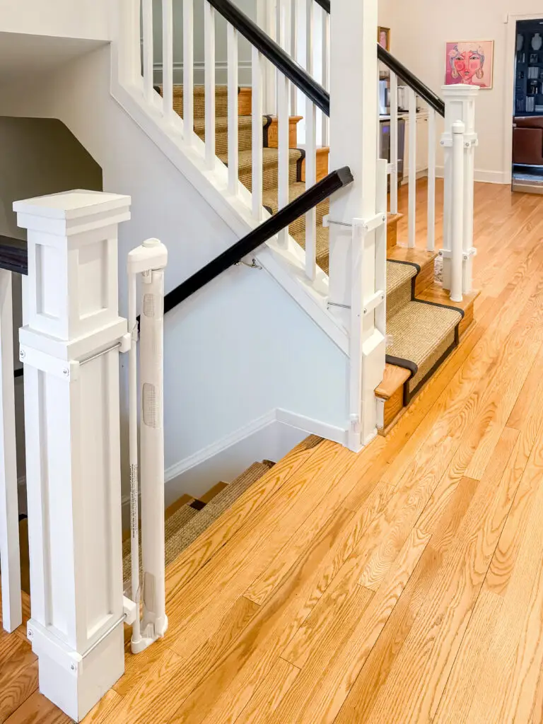 Retractable gate mounted to a square newel post at the foot of the stairs