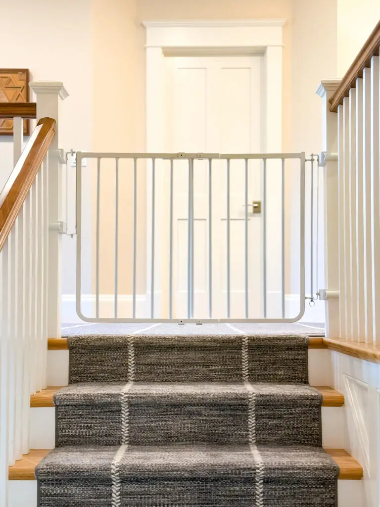 White hardware-mounted baby gate installed at the top of a carpeted staircase