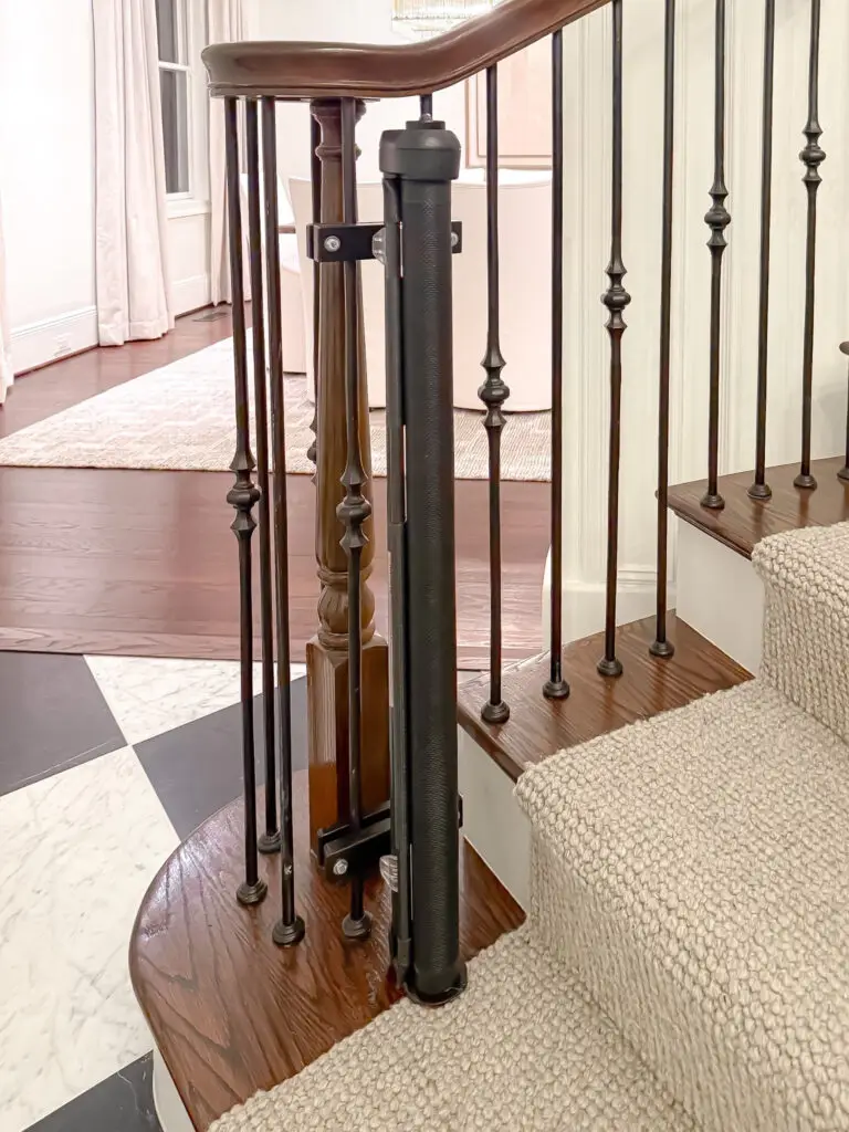 Black post clamp mounted to a wrought iron spindle at the base of the foyer stairs