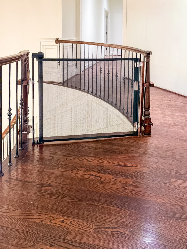 Black retractable gate at the top of the curved staircase with iron balusters on the second floor of a maryland home