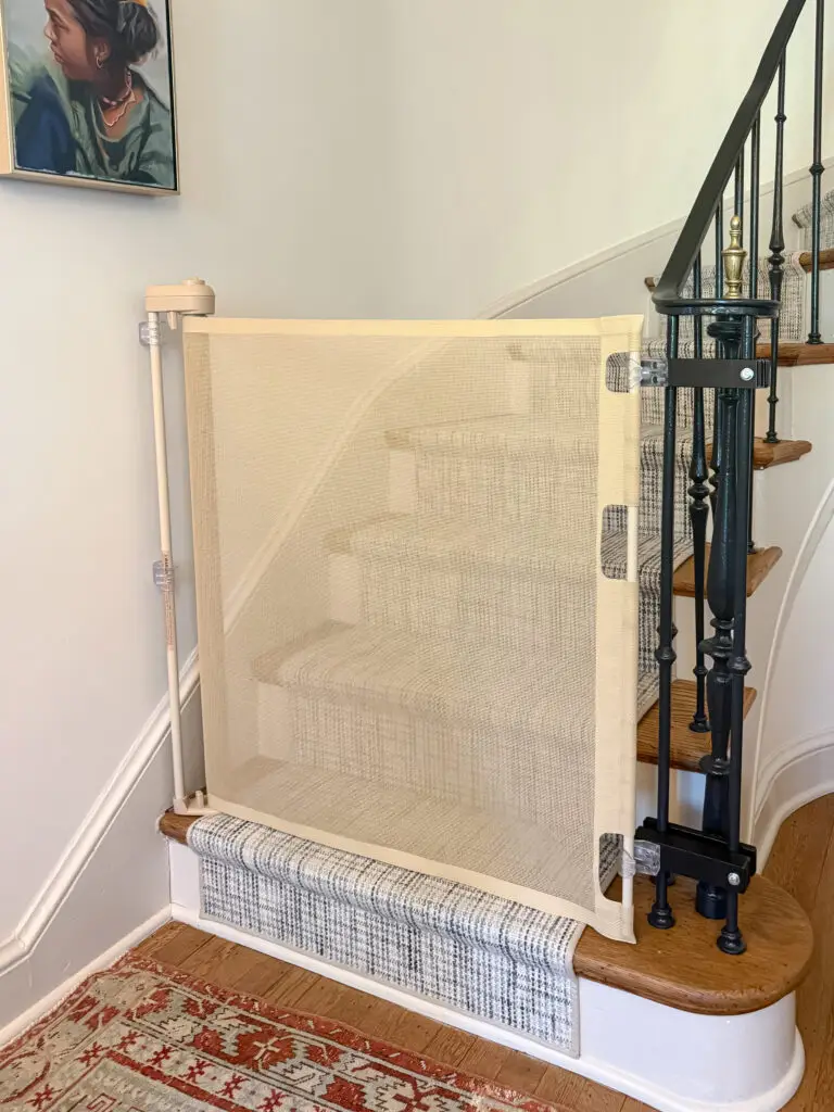 Retractable mesh baby gate at the bottom of a curved dc rowhouse staircase with iron balusters